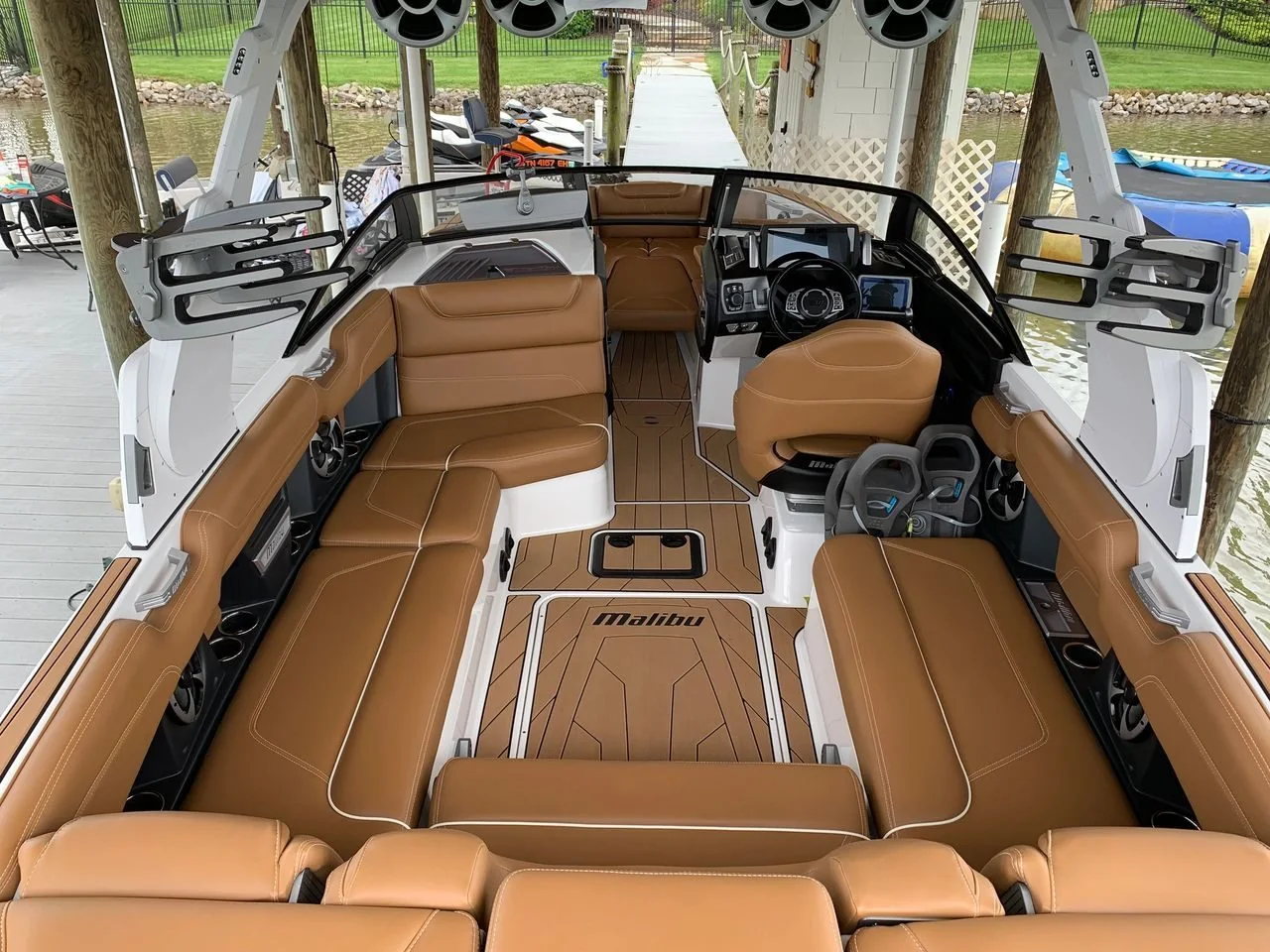 Clean tan leather seating and synthetic teak flooring inside a wake boat at a lake dock